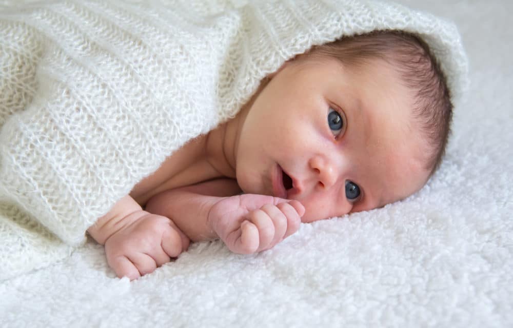 Newborn,Baby,Lies,On,A,White,Plaid,,Covered,With,A